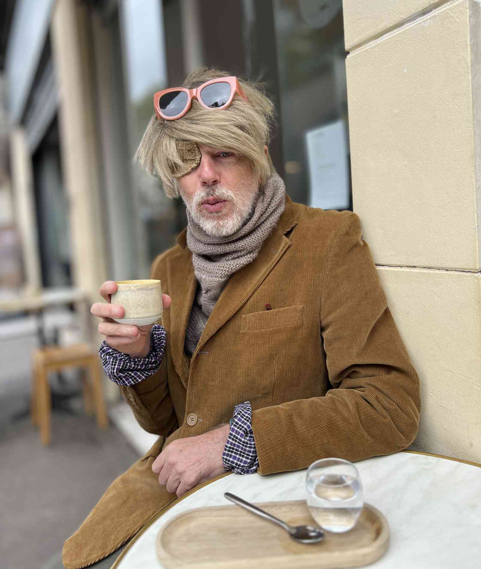 Momus with a hot drink at a pavement cafe